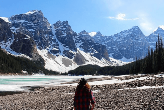 Girl sat beside a lake at the base of mountains in Banff, Alberta