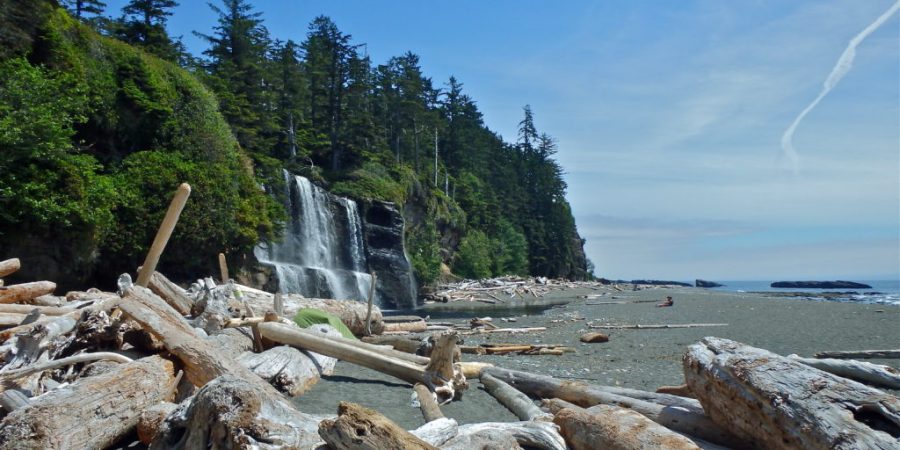A waterfall on a beach with logs in the foreground. Part of the West Coast Trail.