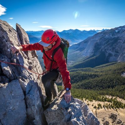 An ACMG rock climber high above a valley with mountains in the background