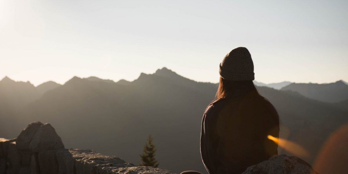 Girl sat on a rock at sunrise, overlooking mountains practicing meditation