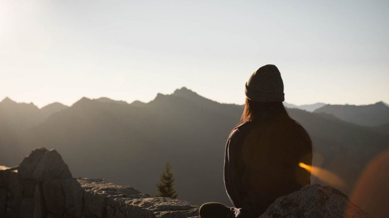 Girl Sat On A Rock At Sunrise, Overlooking Mountains Practicing Meditation