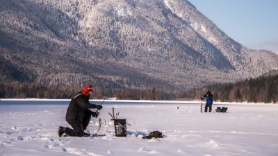 A Person Ice Fishing On A Frozen Lake, With A Snowy Mountain In The Background