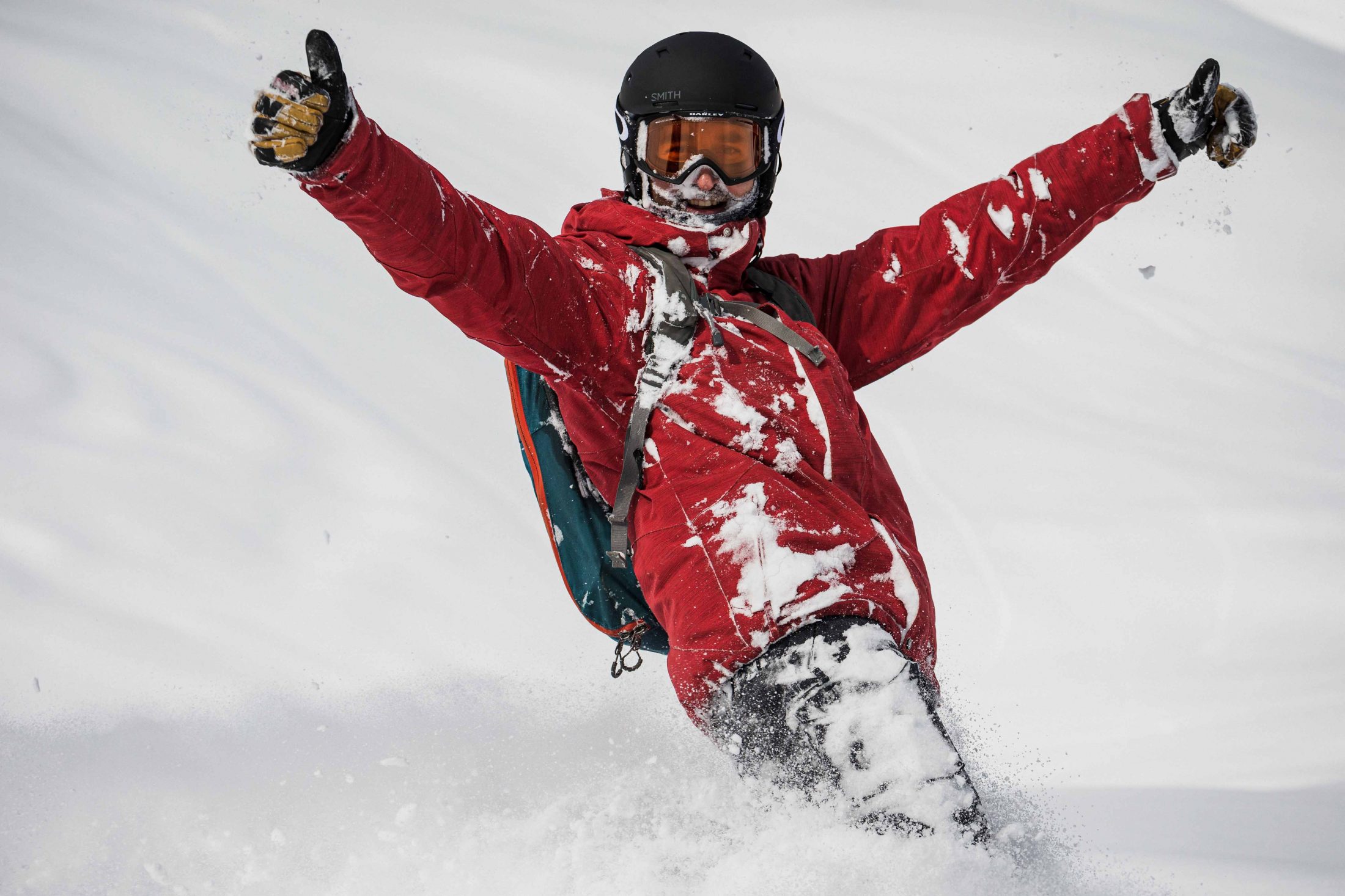 A snowboarder wearing a red jacket giving two thumbs up