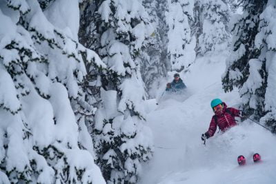 Two People Skiing Through Alpine Terrain In Deep Snow
