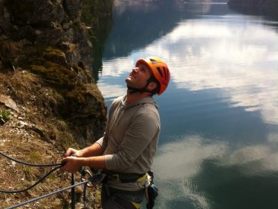A Rock Climber Belays Beside A Lake In Revelstoke BC