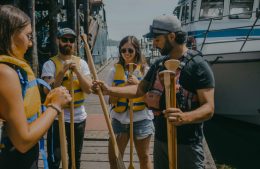A Canoe Guide Hands Paddles To A Group Ready For Adventure