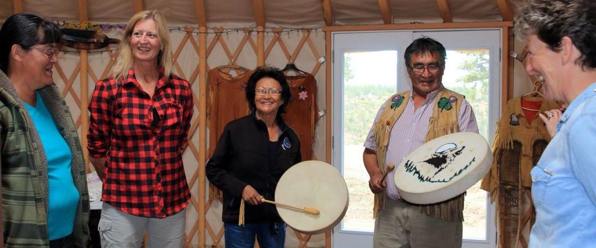 Yukon. Drum Making Workshop. Two people playing drums, three people watching and smiling