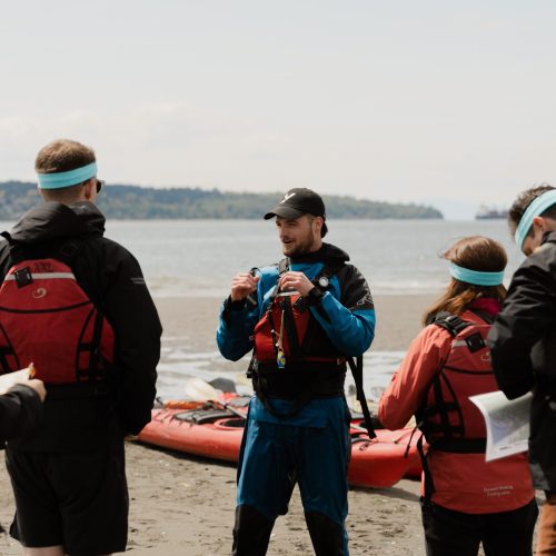 A Kayak Guide Explains A Team Building Activity To A Corporate Group On The Beach In Vancouver, BC